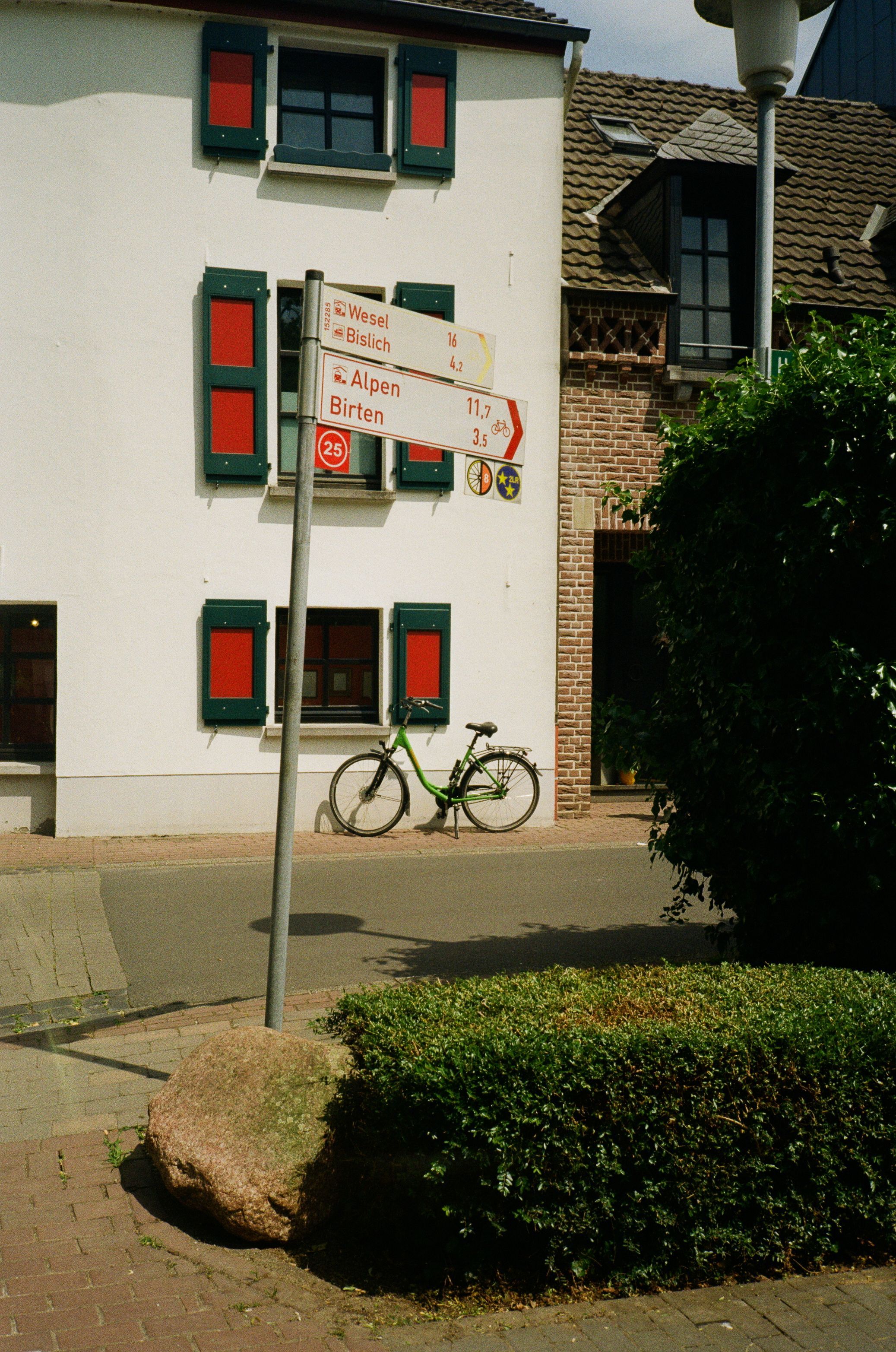 Grünes Fahrrad steht vor Hausmauer mit Straßenschild am Niederrhein.