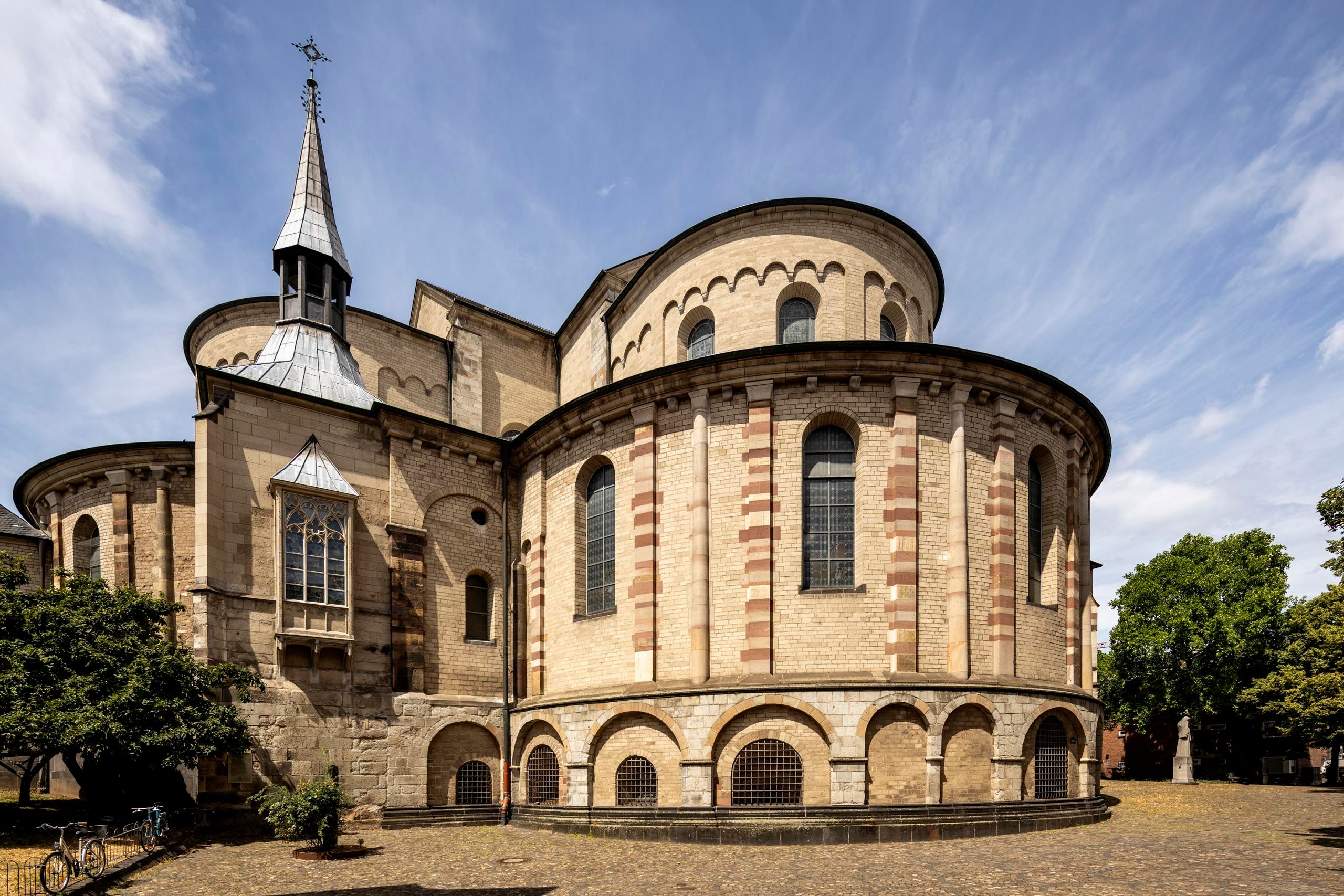 Die romanische Kirche Sankt Maria im Kapitol in Köln mit ihrer markanten Apsis und dem kleinen Turm unter blauem Himmel.