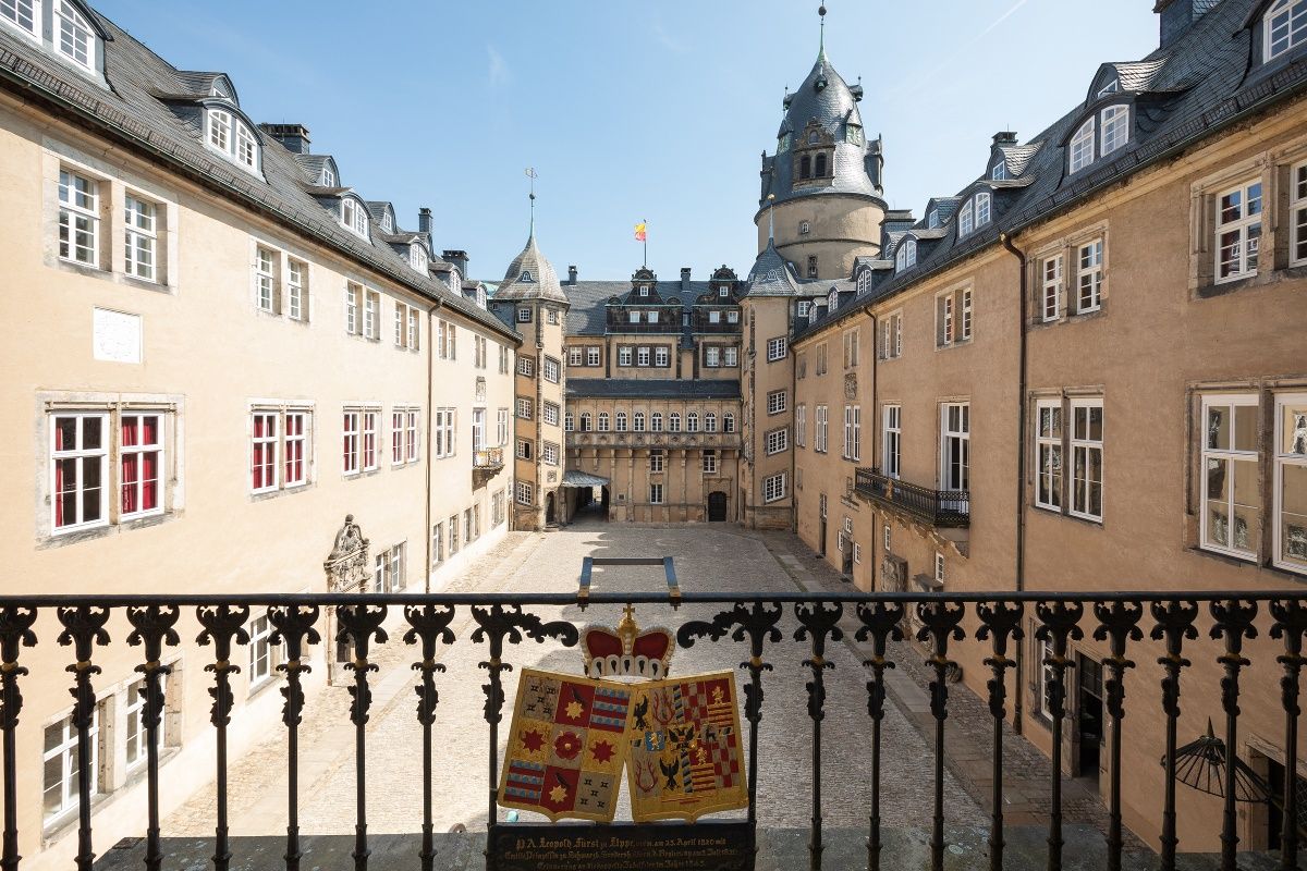 Der Innenhof des Fürstlichen Residenzschlosses Detmold zeigt historische Architektur mit einem Wappen im Vordergrund. Der Himmel ist klar und blau.
