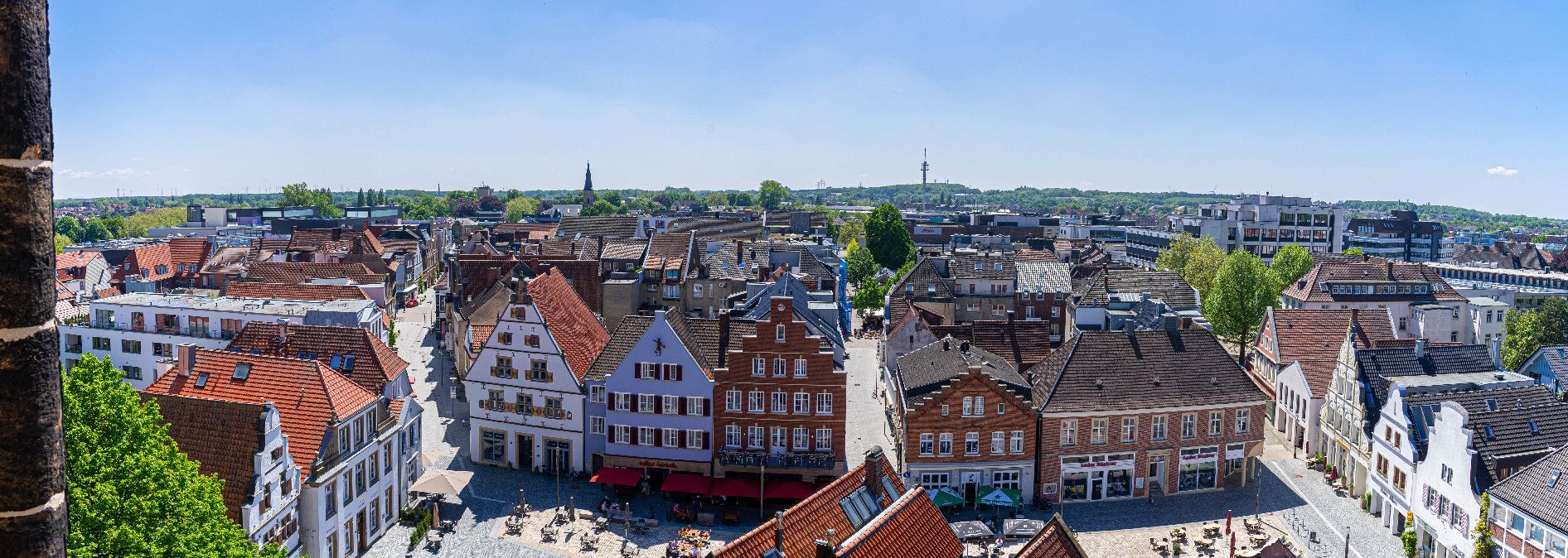 Panoramablick auf den Marktplatz von Rheine mit historischen Gebäuden und einem Kirchturm im Hintergrund.