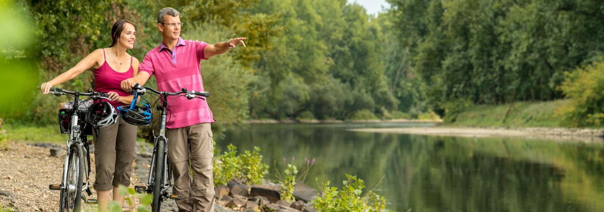 Zwei Personen stehen mit Fahrrädern am Ufer der Niers, umgeben von Bäumen.