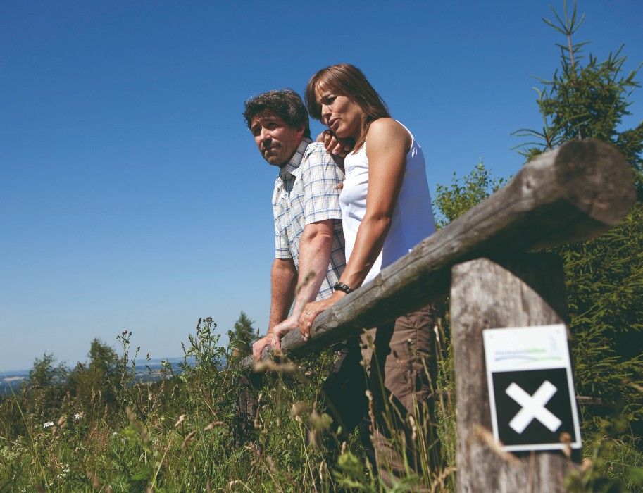 Zwei Personen stehen an einem Holzzaun in einer grünen Landschaft am Eggeweg.
