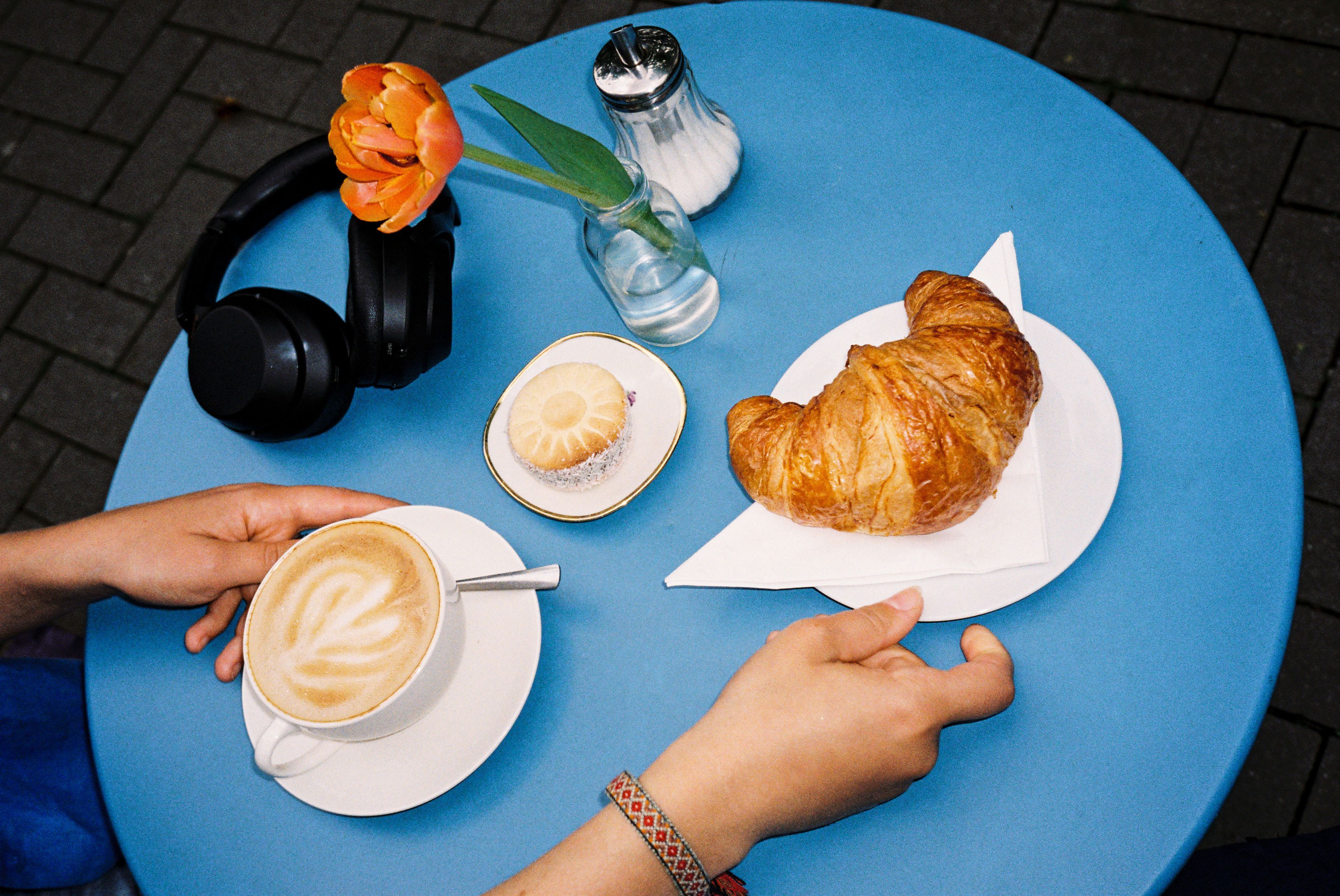 Ein blauer Tisch bestückt mit Kaffee, Blumen und Croissant in Aachen.