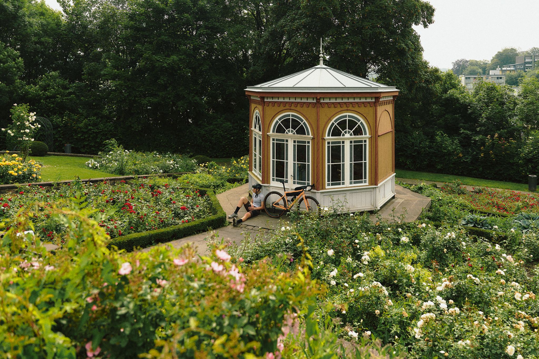 Radfahrende sitzt neben einem Pavillon in einem blühenden Garten.