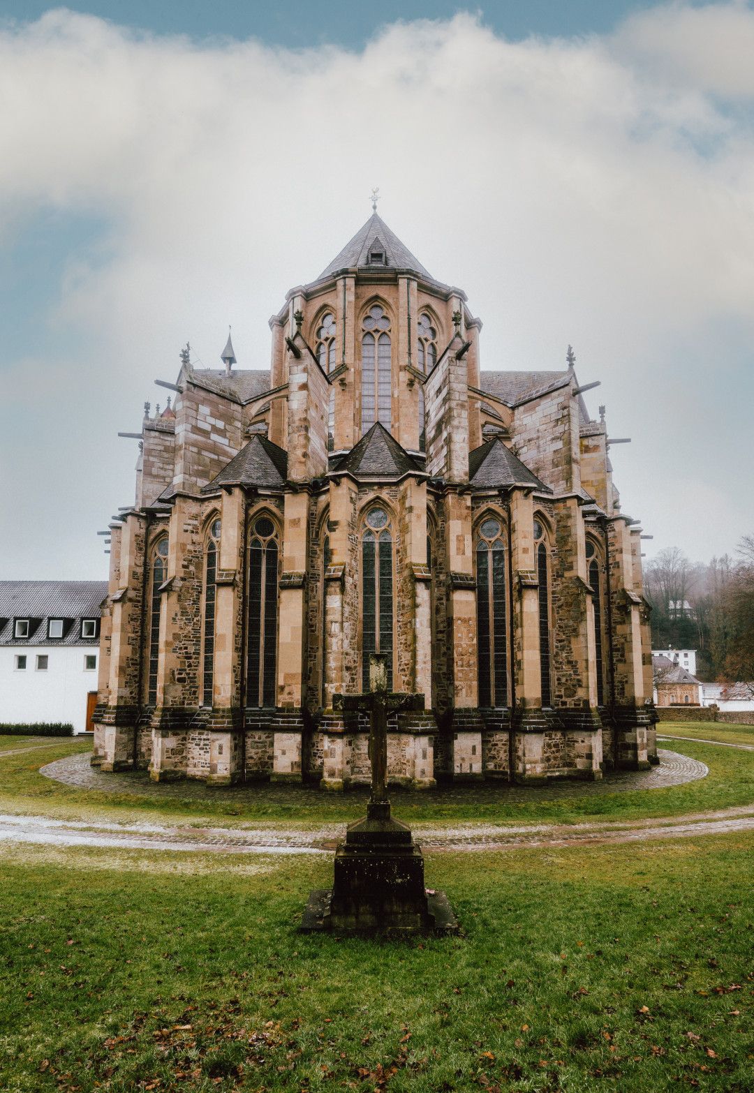 Der Altenberger Dom zeigt seine beeindruckende gotische Architektur mit hohen Fenstern. Ein Kreuz steht im Vordergrund auf einer grünen Wiese.