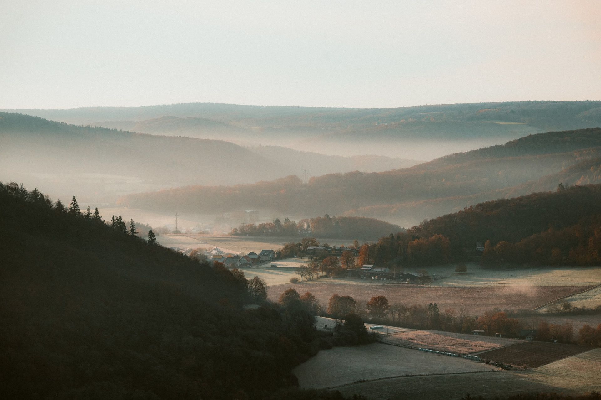 Landschaft mit Hügeln und Nebel in der Ferne, Felder und Bäume im Vordergrund.