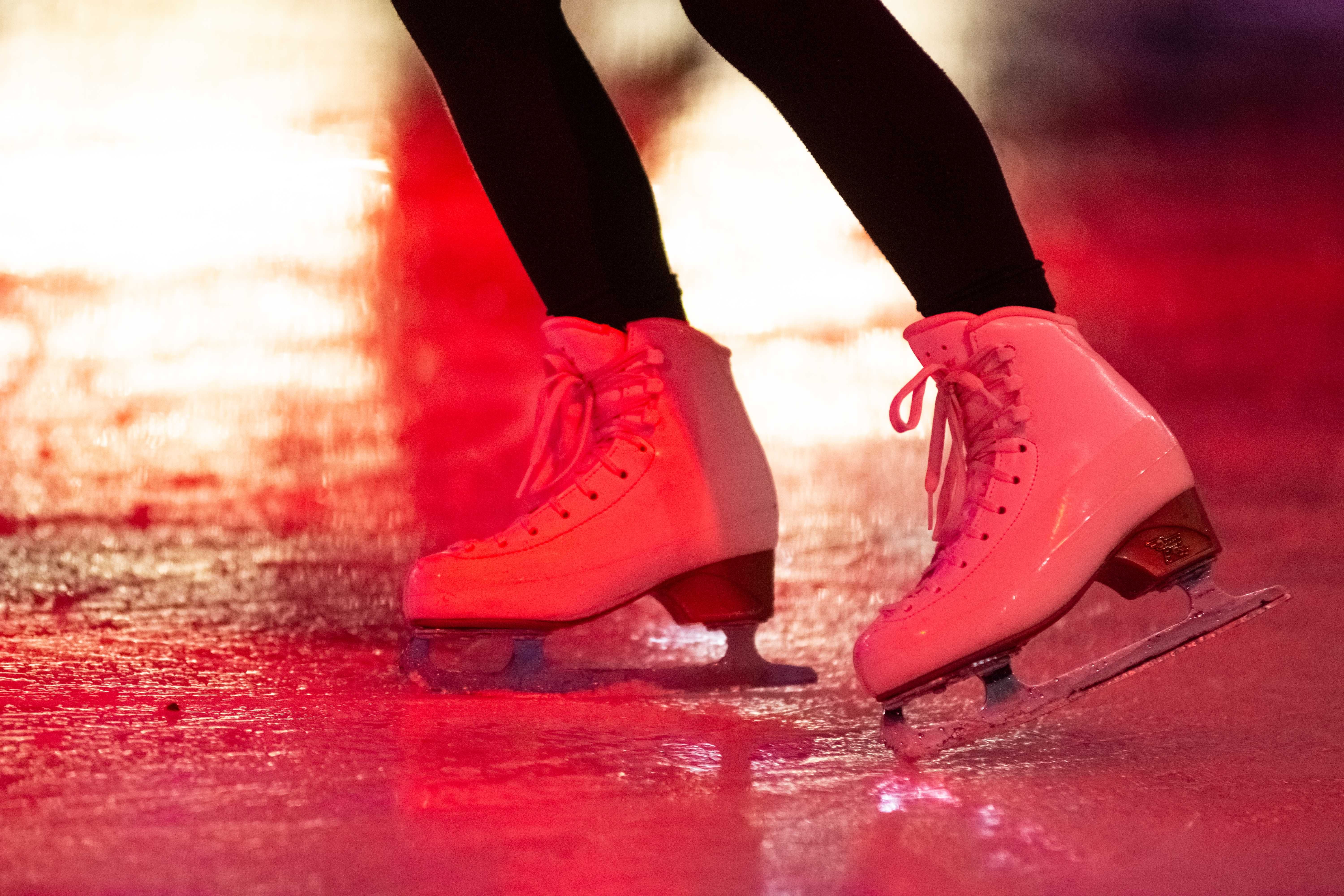 Nahaufnahme von weißen Schlittschuhen auf einer Eisfläche mit rotem Licht.