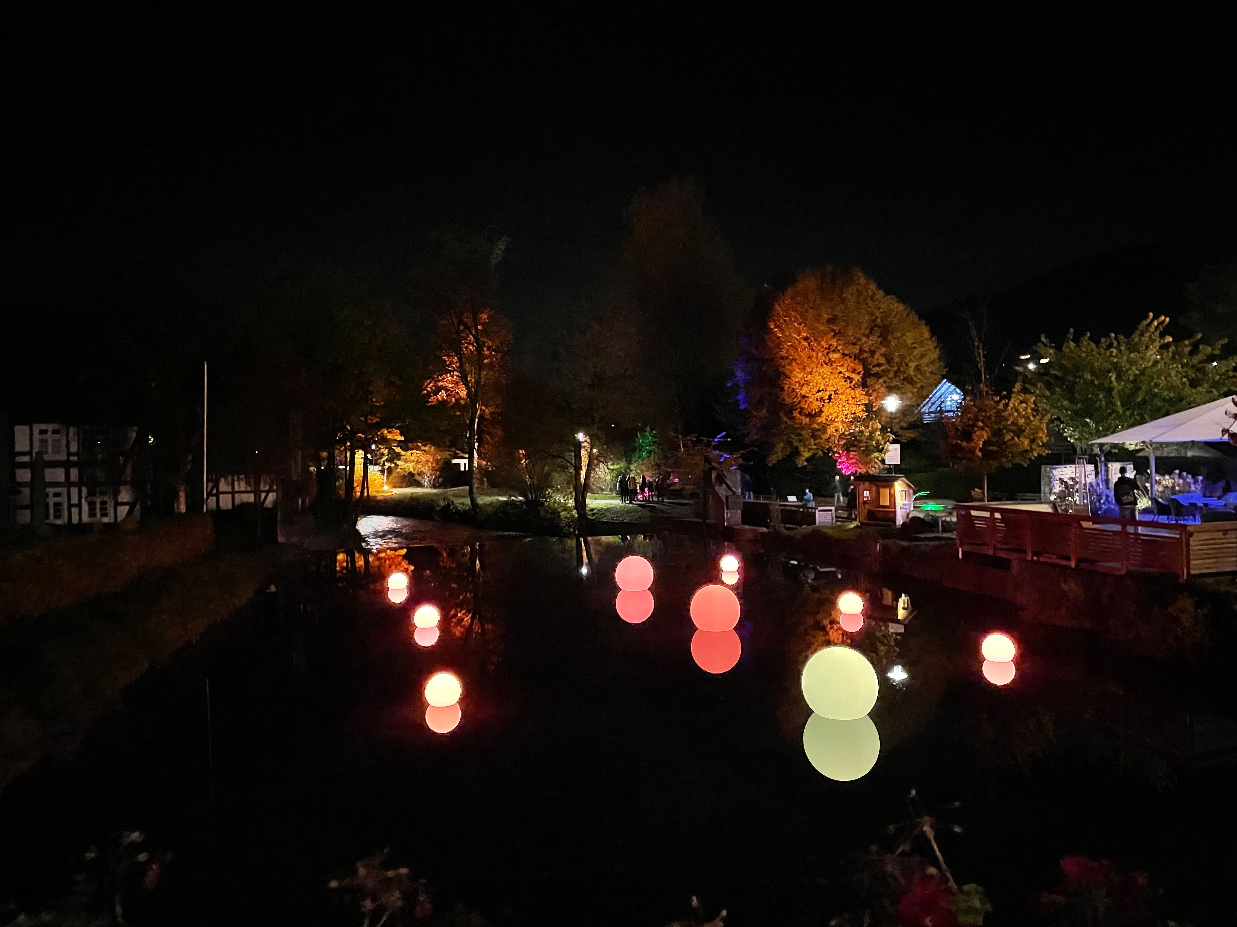 Leuchtende Kugeln schwimmen auf einem Fluss bei Nacht in Lennestadt.