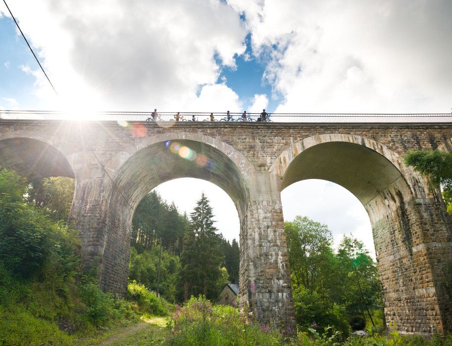 Radfahrer überqueren den Reichensteiner Viadukt der Vennbahn bei Sonnenschein. Der Himmel ist teils bewölkt.