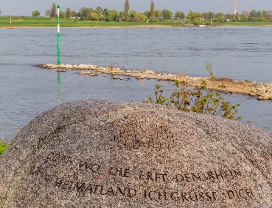 Ein Stein mit Inschrift liegt an der Erftmündung in den Rhein.
