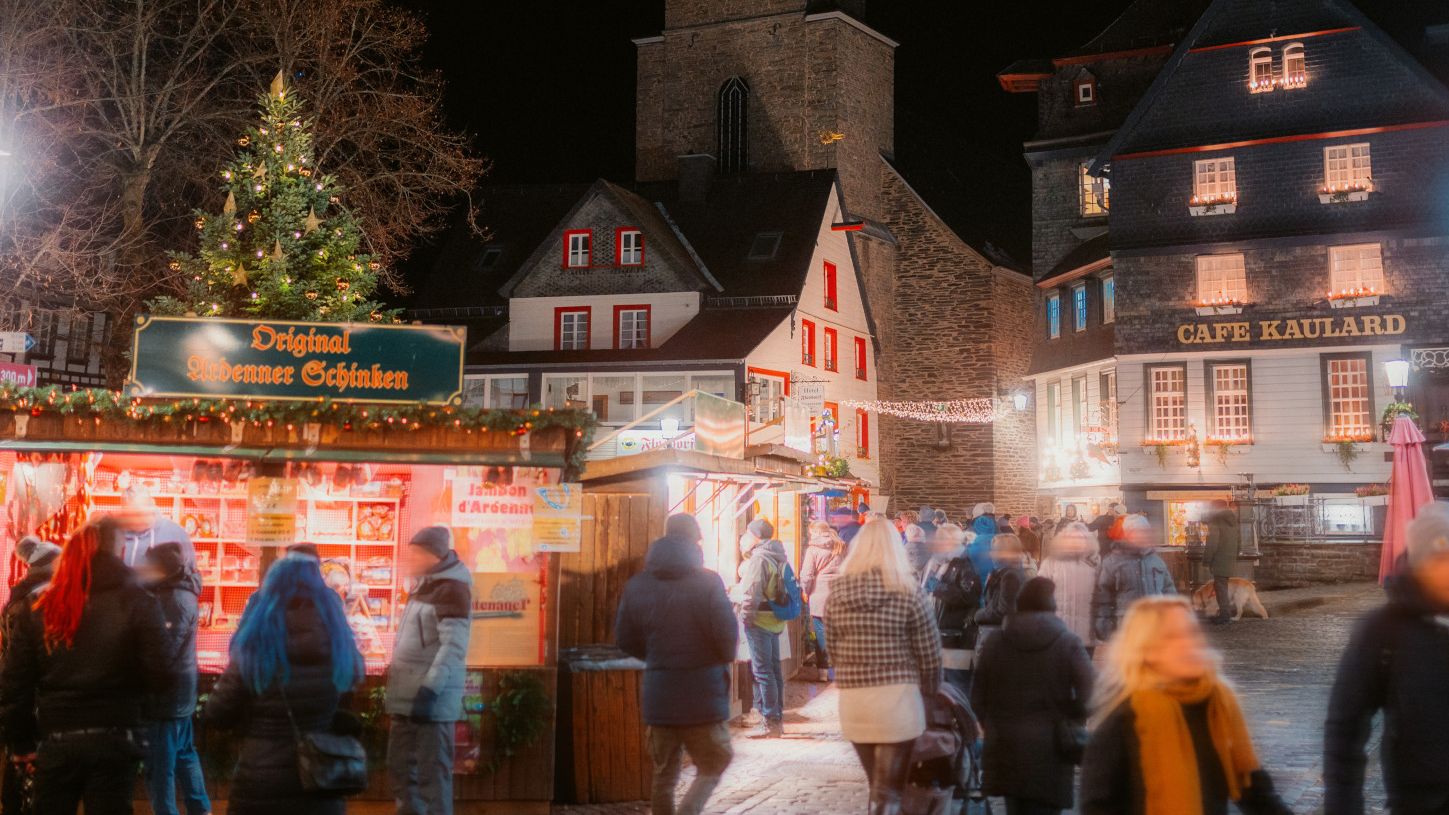Hell erluchtete Buden des Weihnachsmarkts Monschau mit Fachwerkhäusern im Hintergrund
