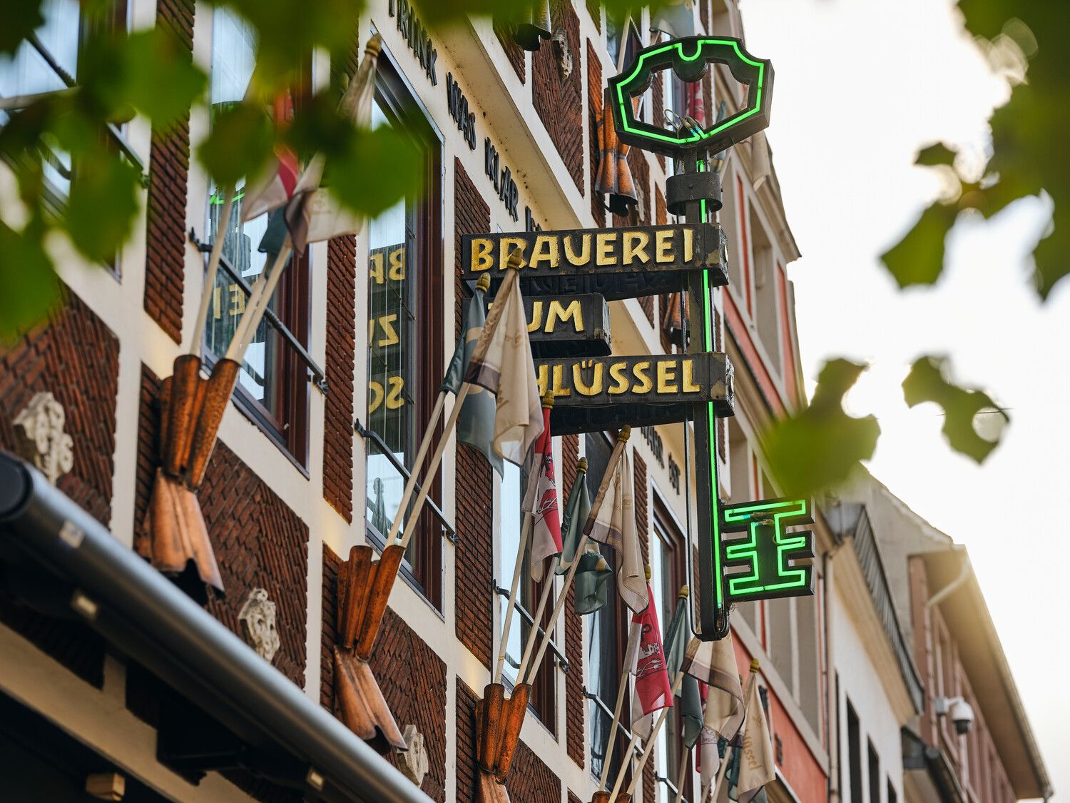 Fassade der Brauerei zum Schlüssel in der Düsseldorfer Altstadt mit leuchtendem Schild und Fahnen.