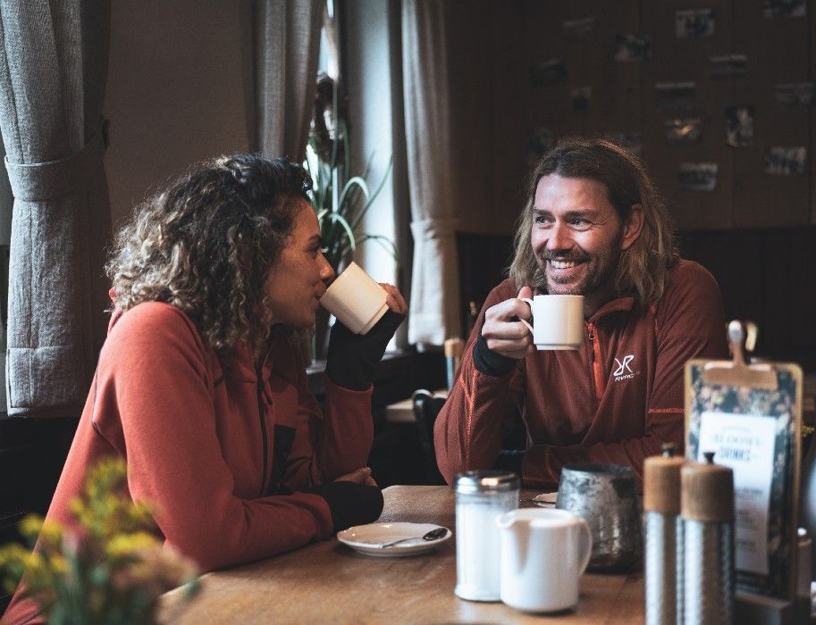 Zwei Personen in Wanderkleidung trinken Kaffee in einer gemütlichen Hütte.