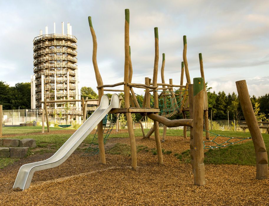 Ein Abenteuerspielplatz mit Klettergerüst und Rutsche, im Hintergrund ein hoher Aussichtsturm.