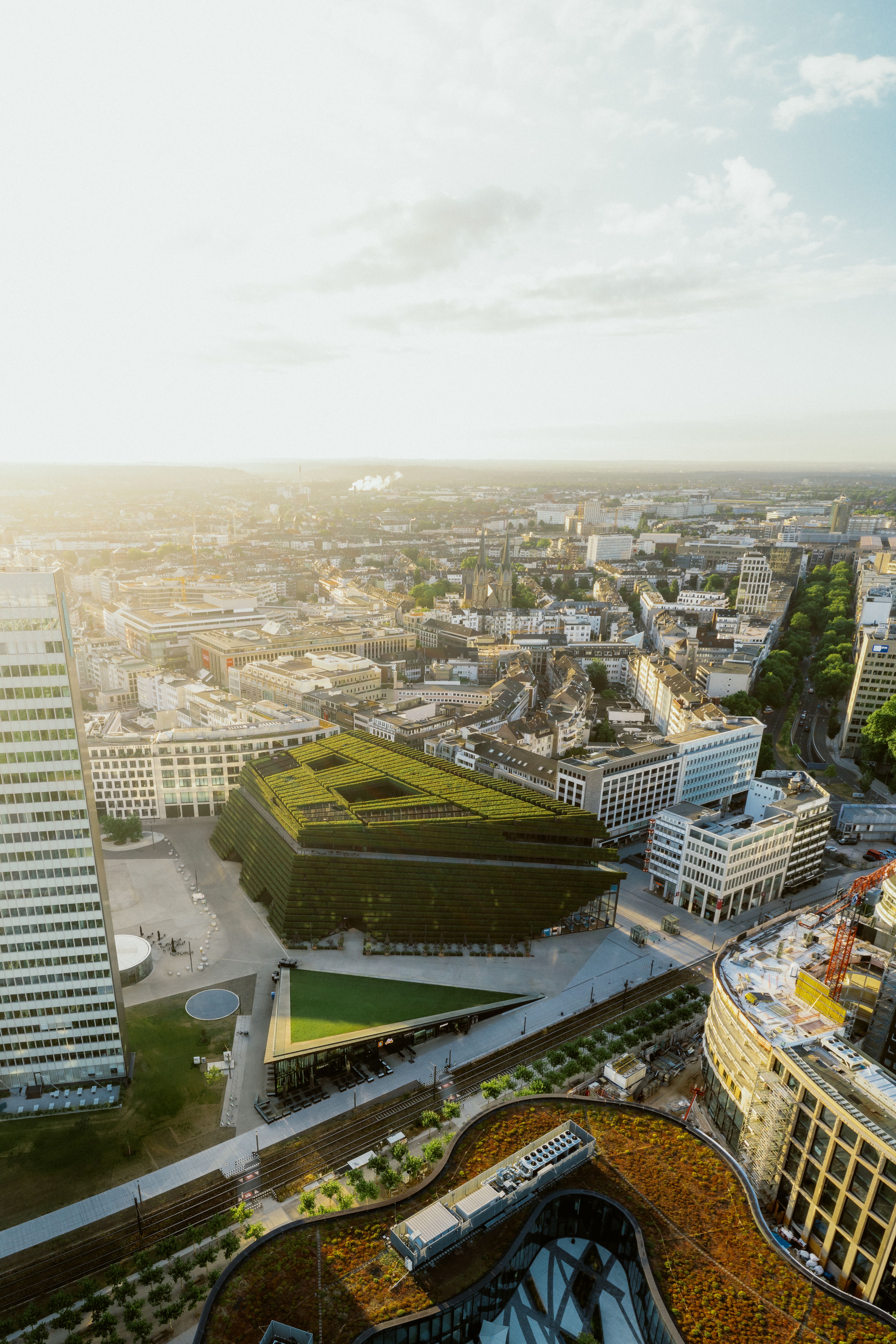 Luftaufnahme des Kö-Bogens in Düsseldorf mit markanten begrünten Dächern und umliegender Stadtlandschaft im Sonnenlicht.