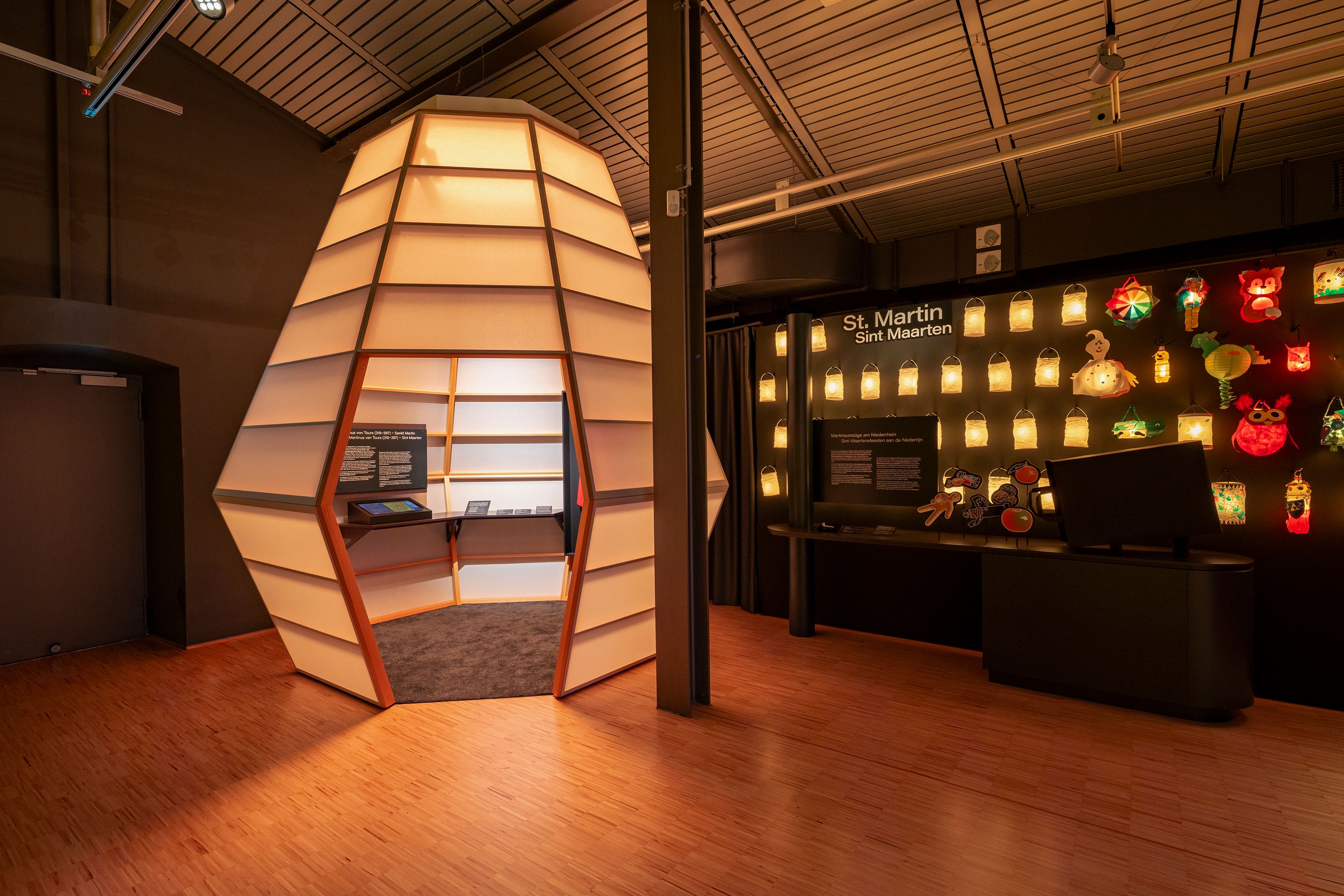 Innenansicht einer Ausstellung mit beleuchteten Laternen und einer großen, beleuchteten Installation in Form eines Kokons.