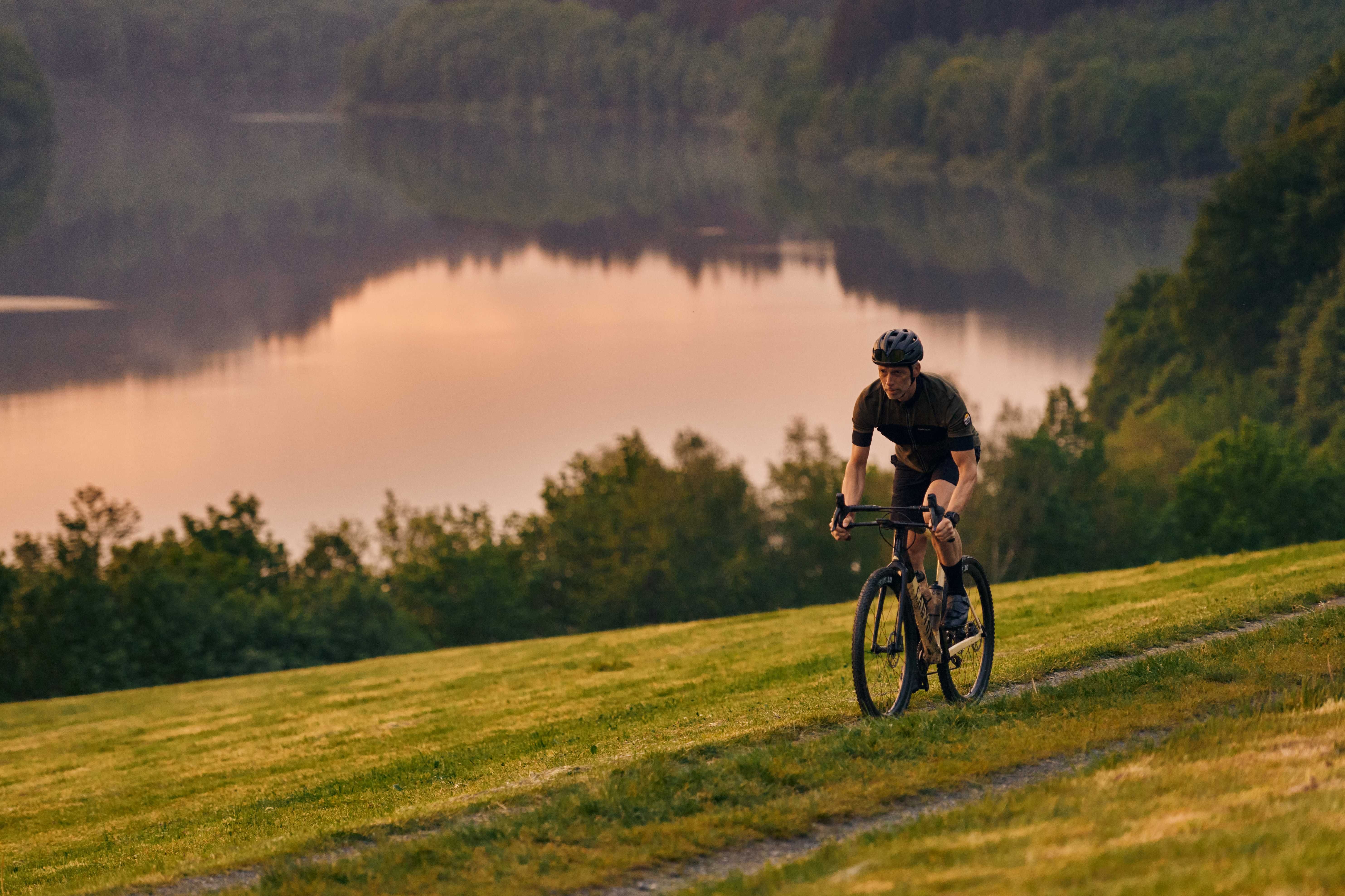 Gravelbiker fährt im Abendliche am Wasser entlang 